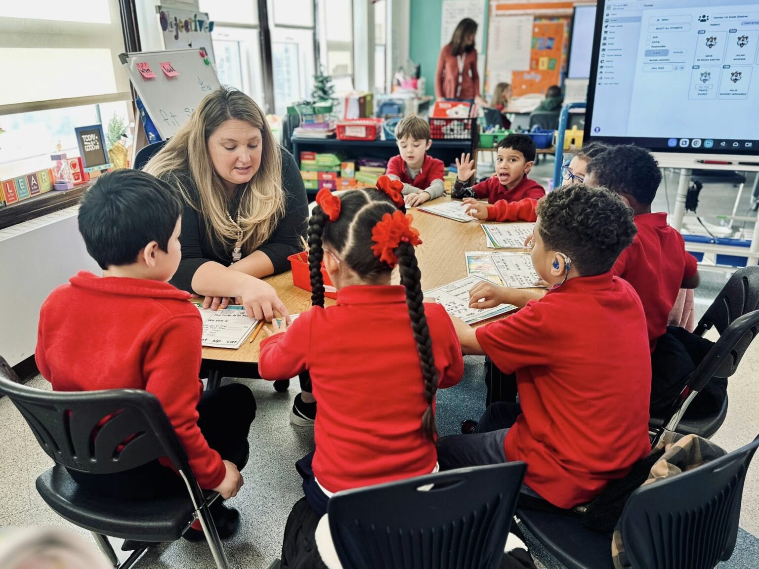 Teacher leading a small-group learning activity with students at Edwin Forrest Elementary School, seated around a table using classroom worksheets and materials.