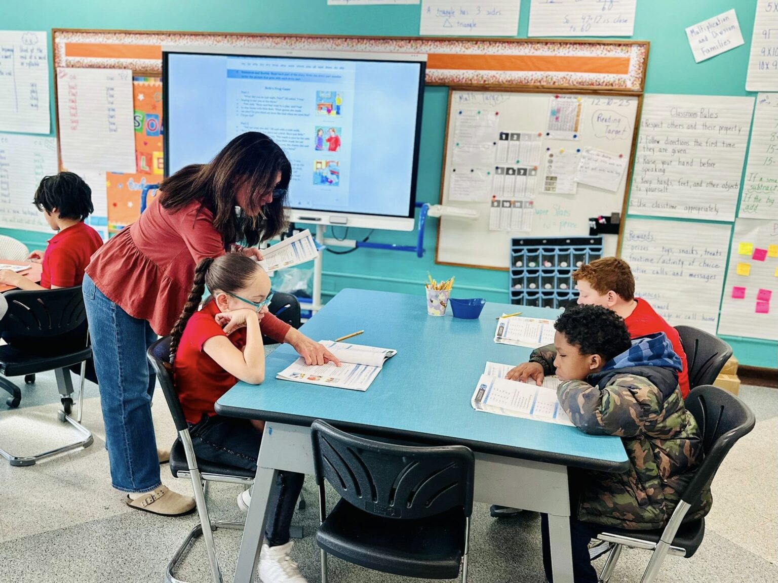 Teacher providing small-group instruction to students at Edwin Forrest Elementary School, with students seated at a table and classroom learning materials visible.